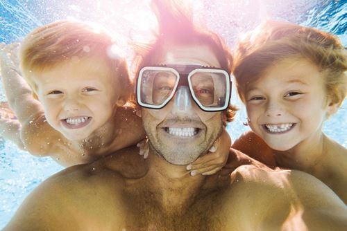 Ein Unterwasserfoto von einem Vater mit seinen beiden Söhnen, der Vater trägt eine Taucherbrille