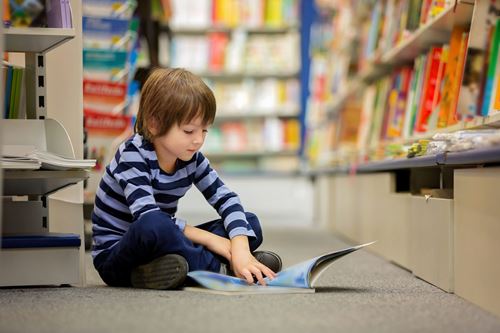 Ein Junge sitzt auf dem Boden einer Bücherei und blättert in einem Buch