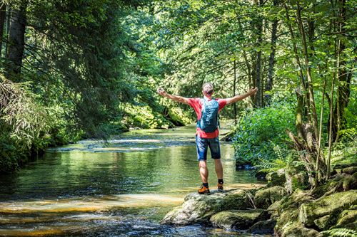 eine Person, die mit ausgestreckten Armen auf einem Felsen in einem Fluss steht